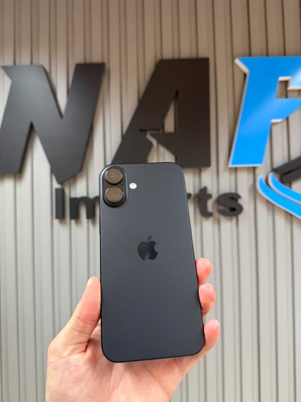 iPhone em frente ao letreiro da NAF Imports na parede da loja